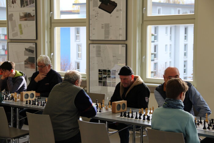 Mehrere Personen an einem langen Tisch die Schach spielen 