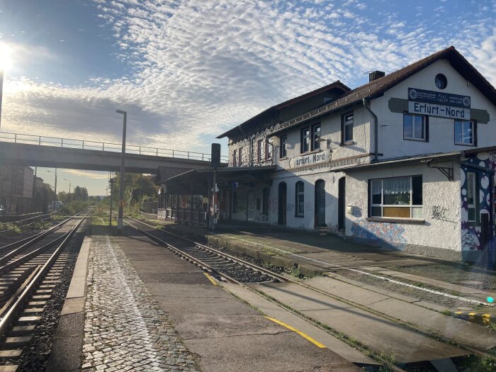 Schienen vor einem Bahnhofsgebäude, im Hintergrund ist eine Brücke zu sehen 